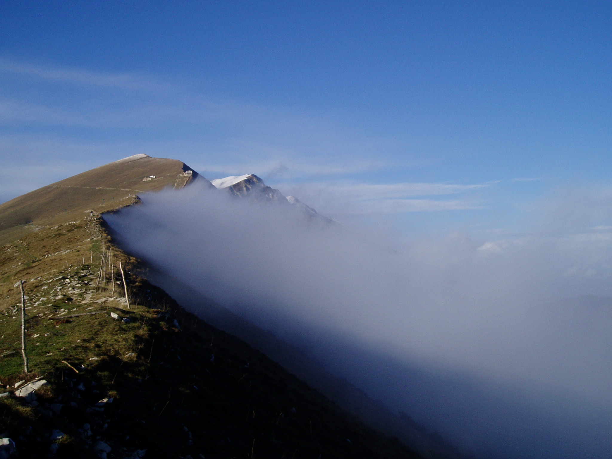 Luglio 2014 - La foto è stata scattata alcuni anni fa sulla cresta meridionale del Monte Baldo guardando verso Nord, in presenza di un forte vento occidentale in quota. Le nubi che si formavano sul versante Val d’Adige (banner clouds)salivano verso l’lalto, e, una volta giunte in cresta, non riuscivano a salire ulteriormente di quota e a valicare la cresta perchè spinte di nuovo verso est e verso il basso dal vento occidentale. L’effetto è ben visibile dalla foto: un confine netto tra nube e aria limpida proprio in prossimità della cresta.
