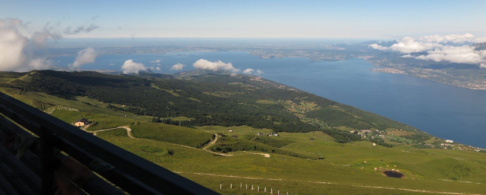 Giugno 2015 - Dopo il passaggio di una debole perturbazione nel giorno precedente, il primo mattino del giorno 24 giugno vede ancora piccoli strati nuvolosi a bassa quota in dissolvimento sui monti circostanti il Lago di Garda. Tale nuvolosità si dissolverà poi entro metà mattina, grazie al riscaldamento solare, per poi riformarsi nel pomeriggio sulle cime del Baldo. Nella foto, scattata dal Rifugio Chierego da Matteo Calzà, si vede anche l’Osservatorio Meteorologico Rifugio Fiori del Baldo sulla sinistra.