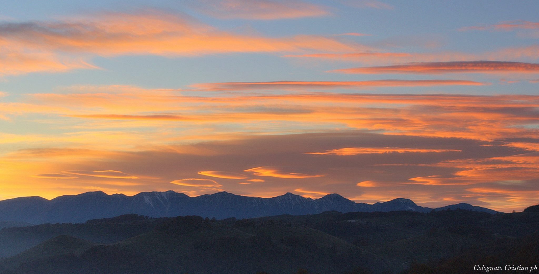 Ottobre 2015 - Per il mese di ottobre vi proponiamo uno scatto in cui vediamo nubi lenticolari e cirrostrati sul Monte Baldo al tramonto (foto Colognato). Le nubi lenticolari, dette anche lee-clouds, si formano tipicamente sottovento alle Alpi con correnti settentrionali o nord-occidentali in alta quota.